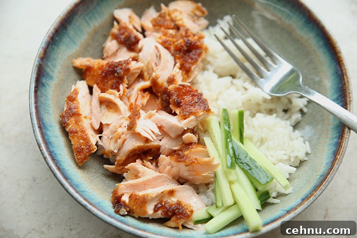 A dinner plate with a serving of smoky brown sugar salmon, sliced cucumbers, and coconut rice. A fork is inserted diagonally from the left into a flaky piece of salmon.