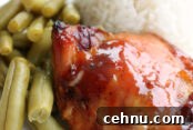 A white plate with a serving of green beans, white rice, and a sweet and sour chicken thigh.