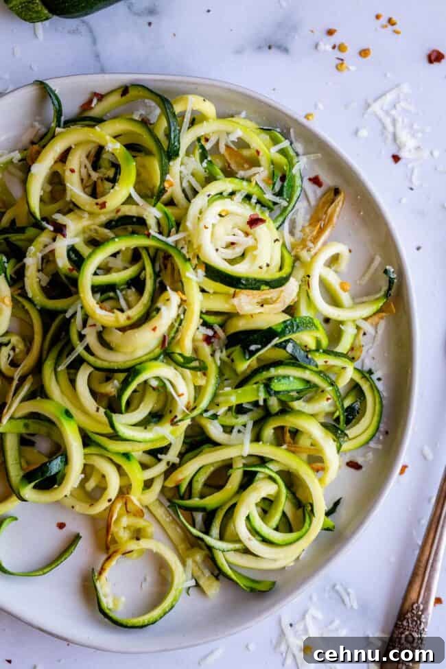 Zucchini noodles on a white plate with spices and cheese.