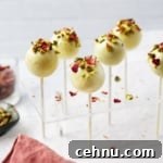 Pistachio cake pops coated in white chocolate topped with chopped pistachios and dried rose petals displayed in acrylic cake pop stand