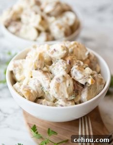 potato salad served in small white bowl on wooden board with second bowl blurred in background
