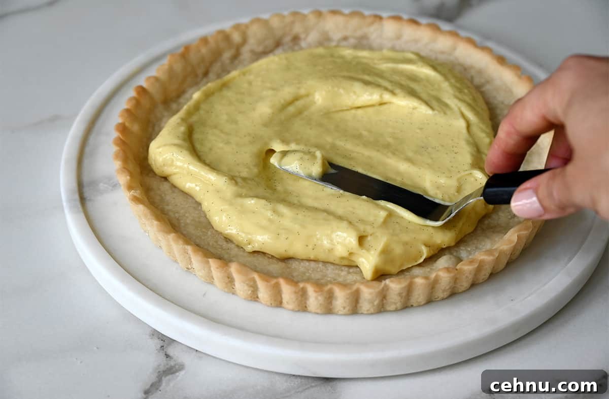 Vanilla pastry cream being spread atop a shortbread crust with an offset spatula.