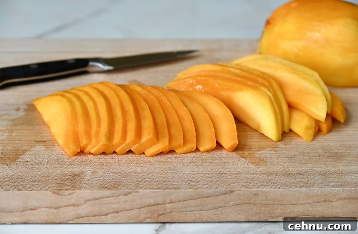 Thin slices of mango on a cutting board next to a sharp knife.