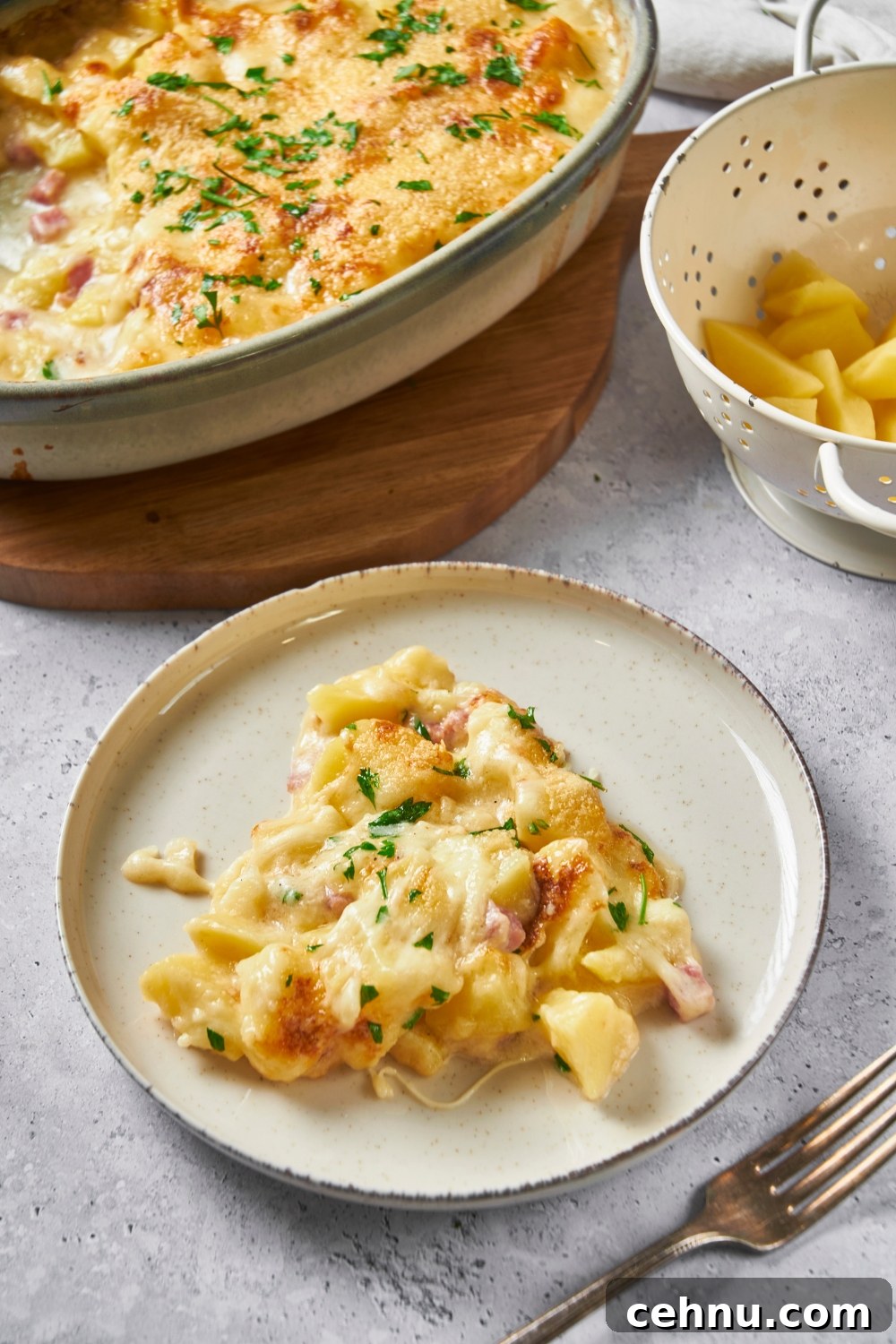 White plate with ham and potato casserole garnished with fresh parsley.