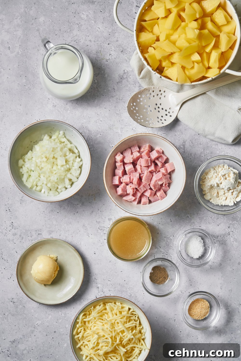 An assortment of ingredients including bowls of diced onion, diced potatoes, cubed ham, shredded cheese, and butter.