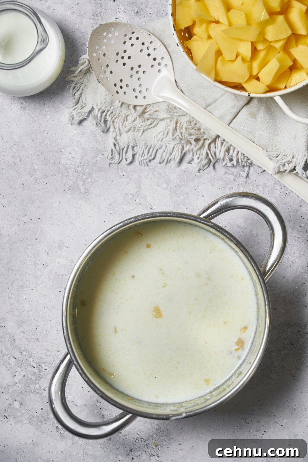 Sauce pot filled with a creamy sauce, and a bowl of cubed potatoes and a slotted spoon in the corner.