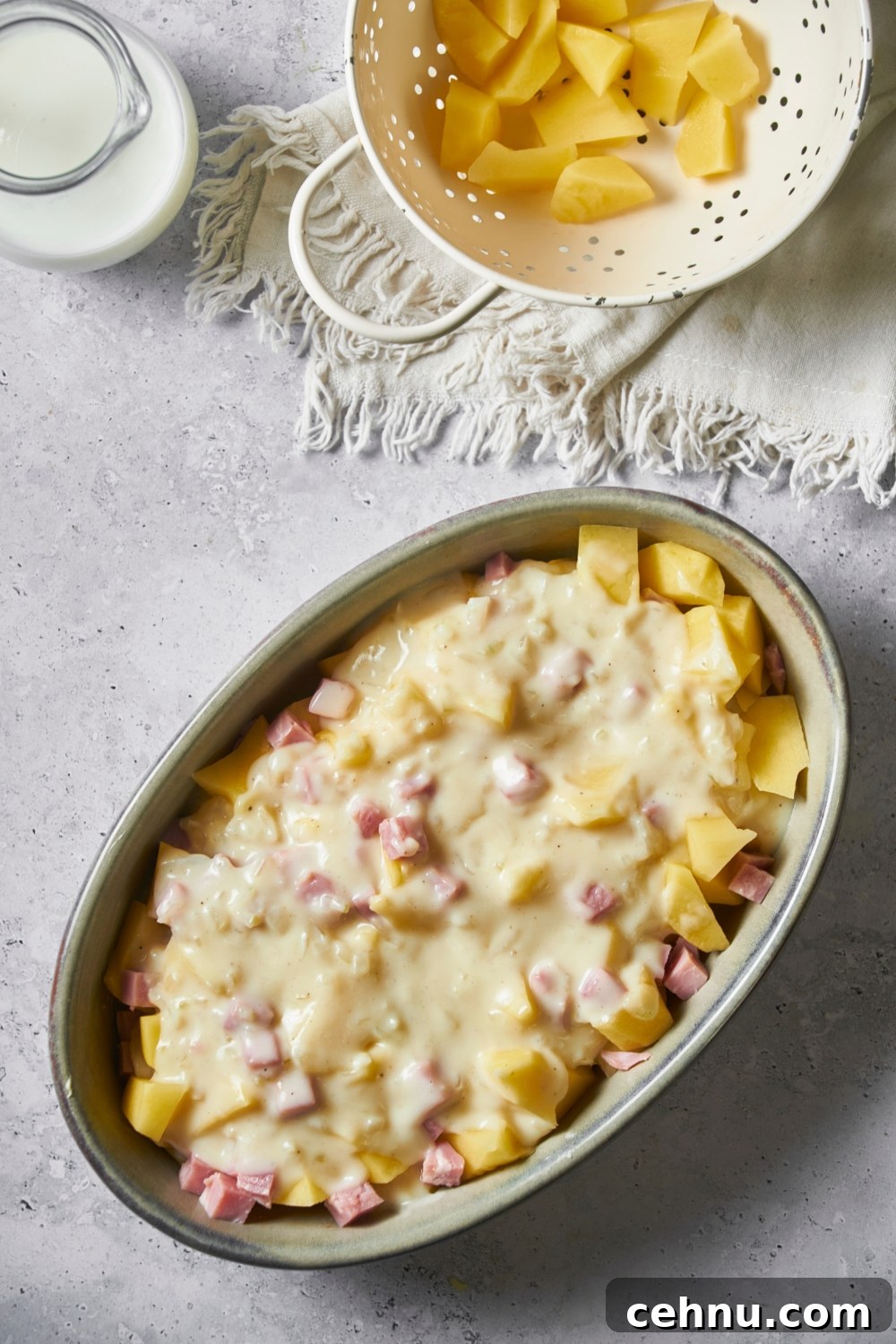 Uncooked ham and potato casserole covered in a creamy sauce in a large casserole dish.