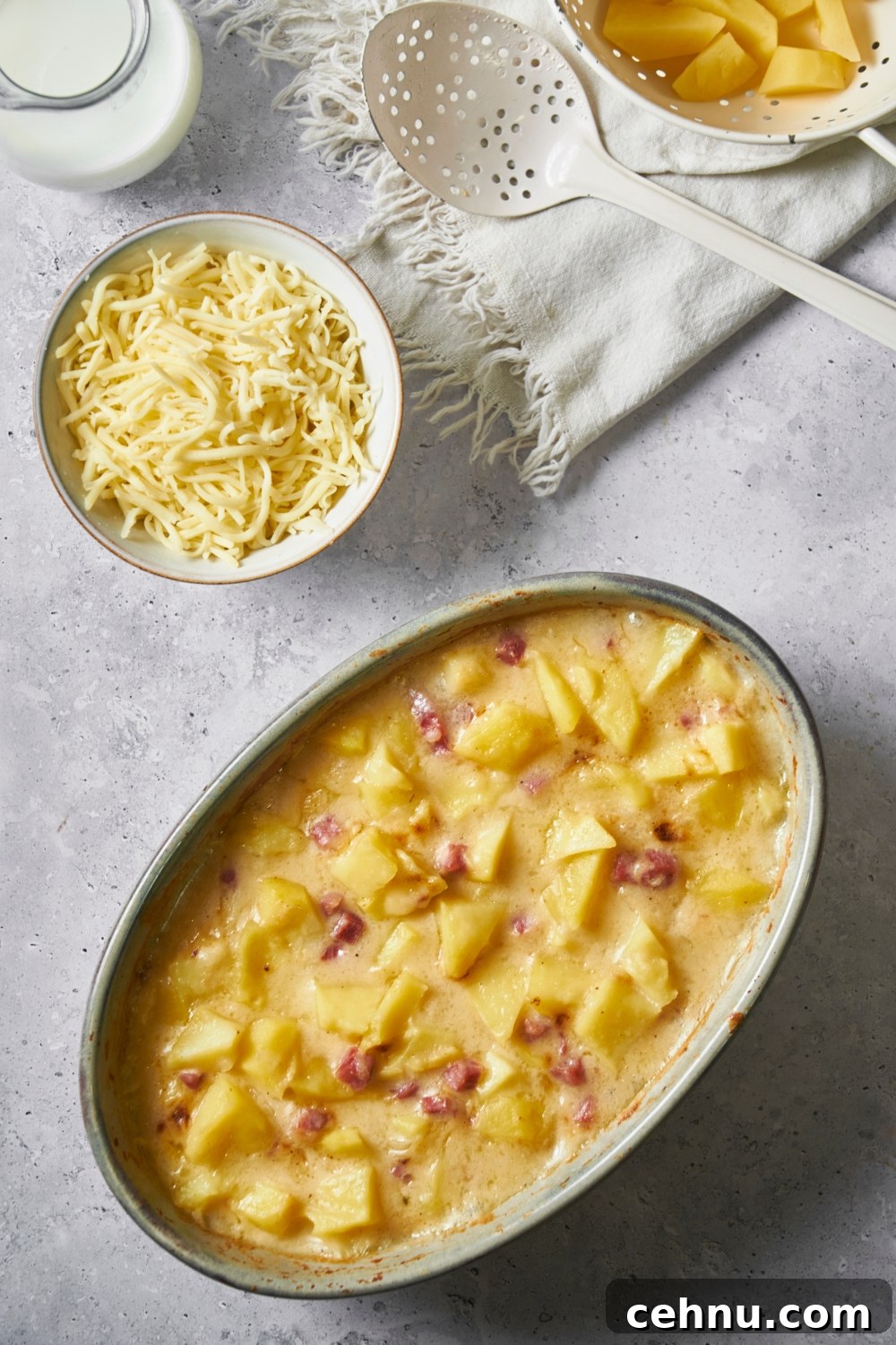 Ham and potato casserole in a large casserole dish, with a bowl of shredded cheese next to the casserole dish.