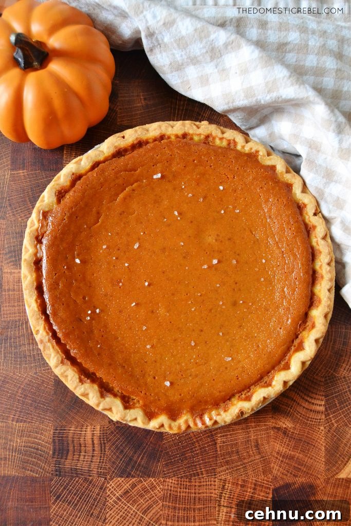 Salted Caramel Pumpkin Pie Recipe for Thanksgiving 4 a whole salted caramel pumpkin pie on a wood board next to a dishtowel and a mini pumpkin