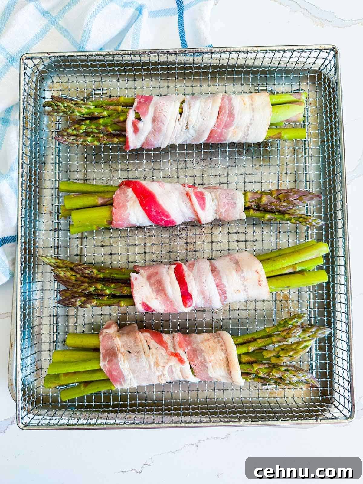Bacon wrapped asparagus in an air fryer basket before cooking.