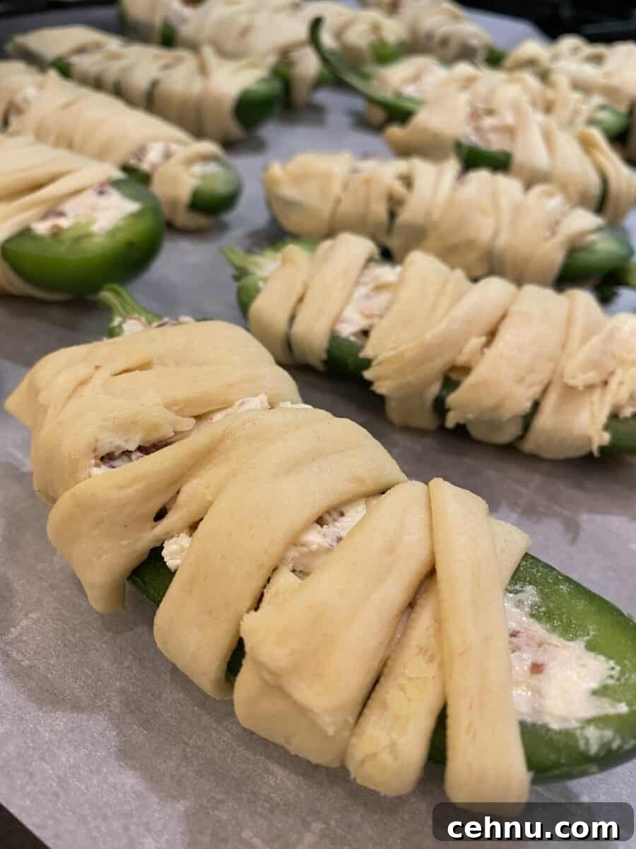 Bacon Wrapped Jalapeno Popper Mummies 3 Unbaked jalapeno halves wrapped in crescent dough on a baking sheet.