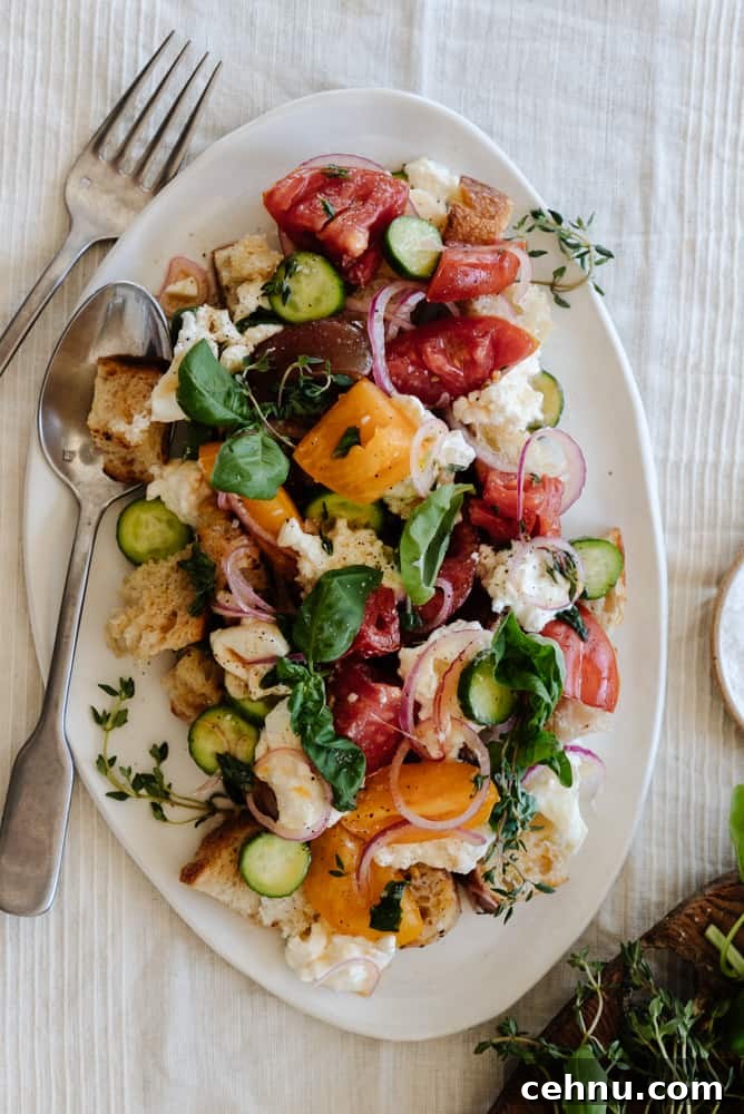 panzanella salad on a white platter on a linen tablecloth with a fork and knife leaning on the platter