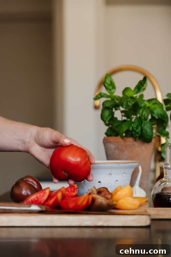 hand grabbing a fresh tomato with cut tomatoes on a cutting board with fresh herbs in a vase in the background