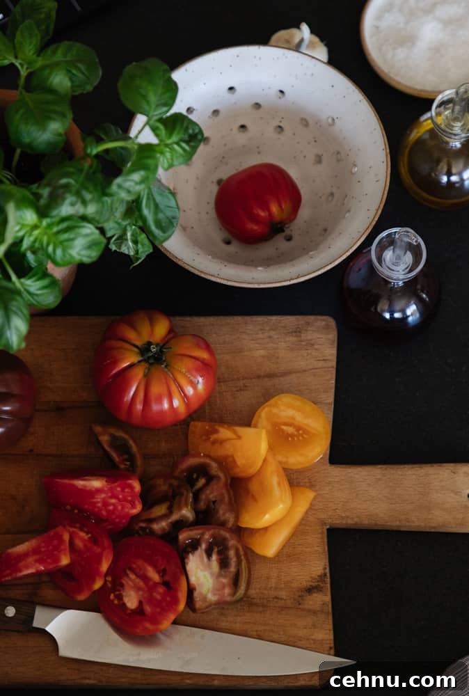 top view of heirloom tomatoes being sliced on a rustic wood cutting board with a colander and basil plant