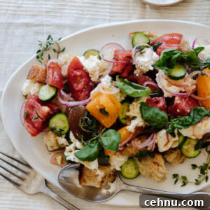 fork and spoon laying on a white platter filled with panzanella salad