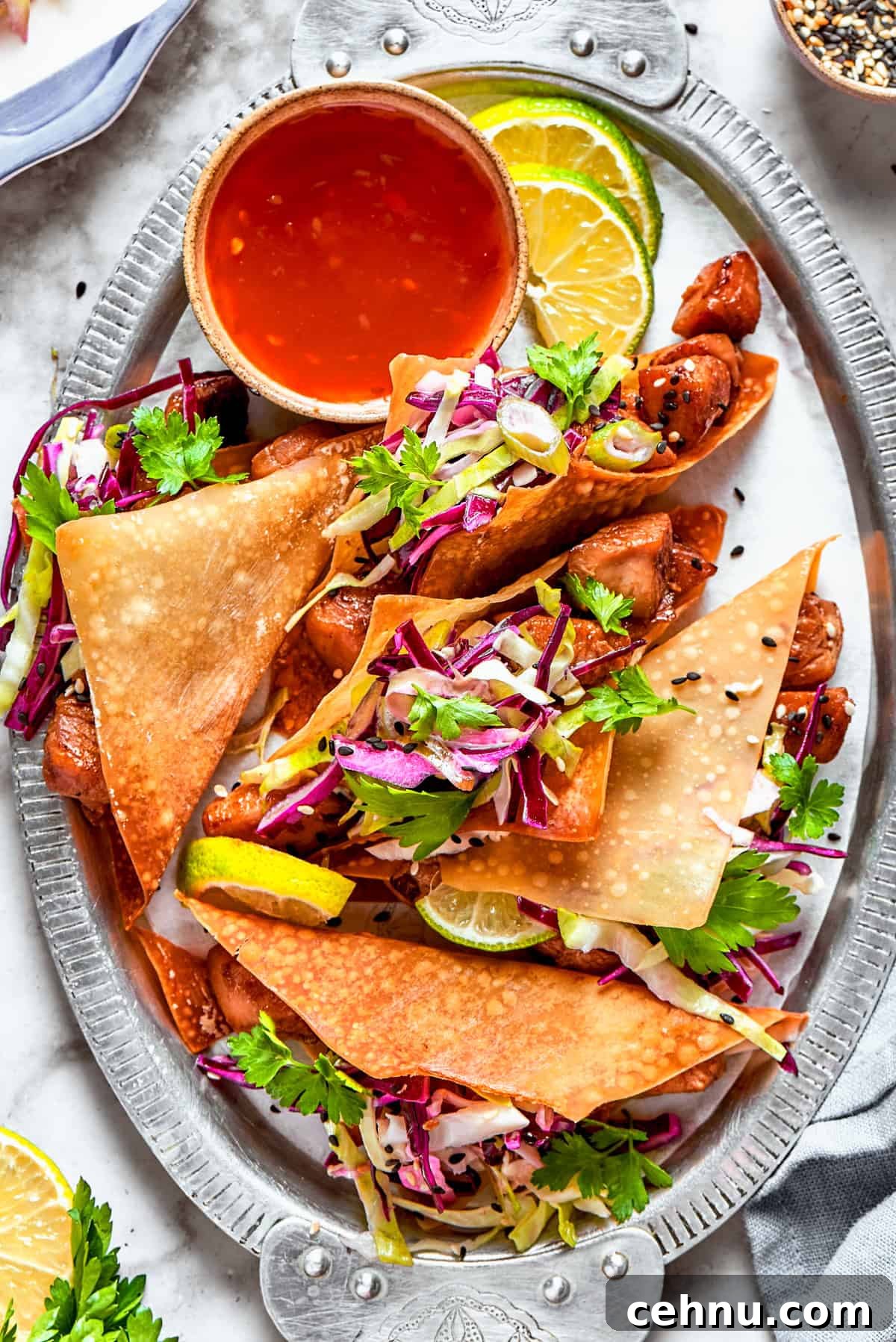 Chicken wonton tacos arranged on an oval platter with a bowl of sauce set right next to the tacos.