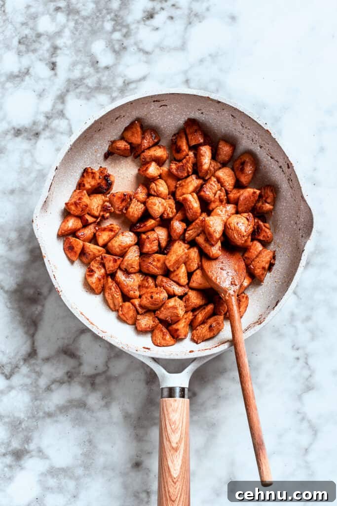 A spoon stirs the chicken as it browns and cooks in the skillet.