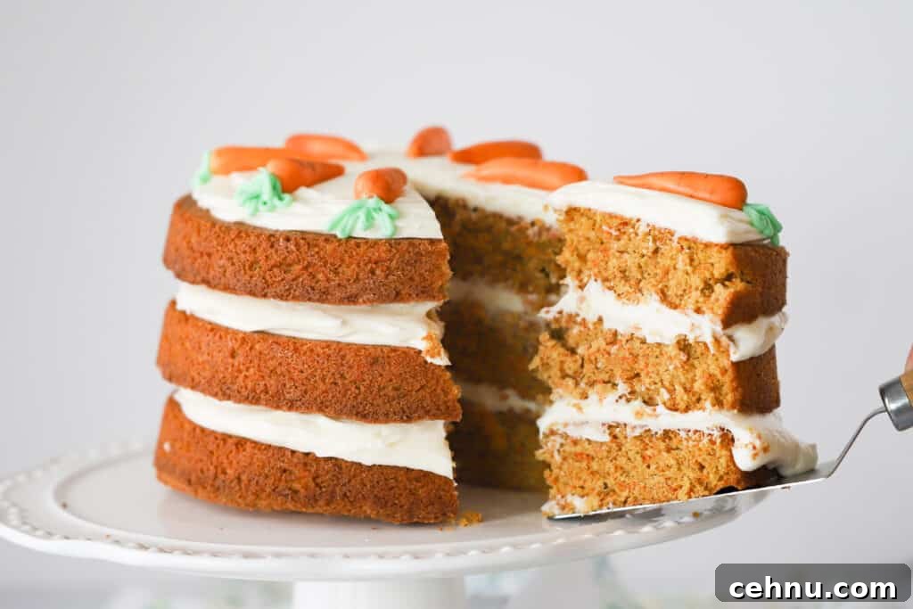 A three-tiered Carrot Cake with cream cheese frosting on top of the cake and in between the layers.  A slice is being removed using a cake server.