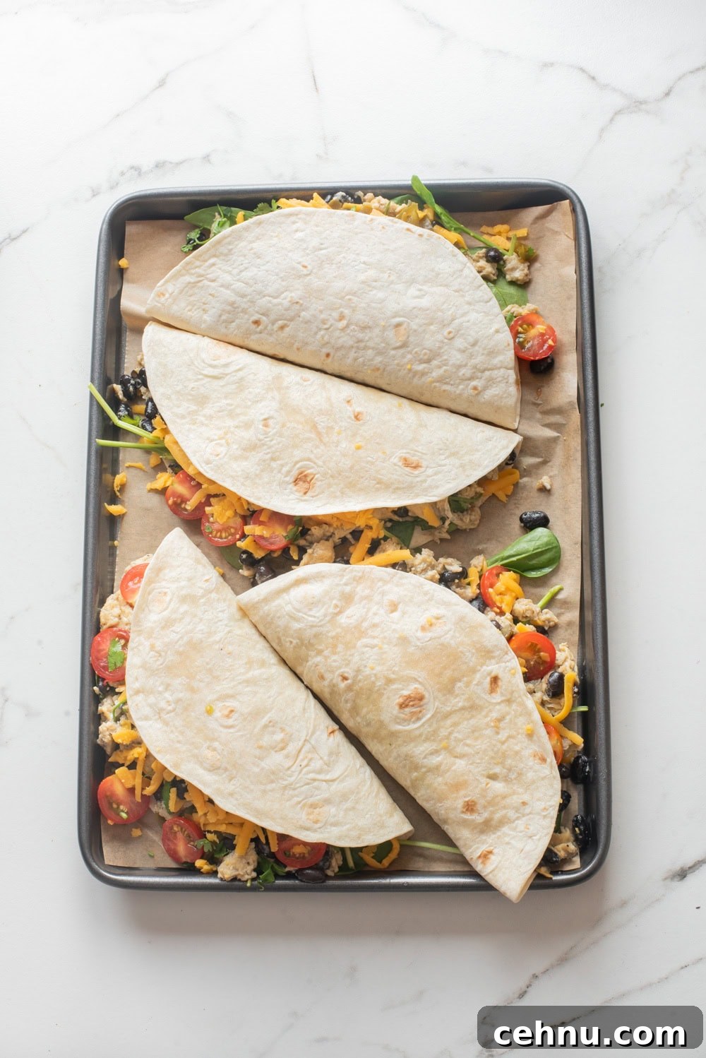 An overhead image of four breakfast quesadillas on a sheet pan, ready to ba baked.