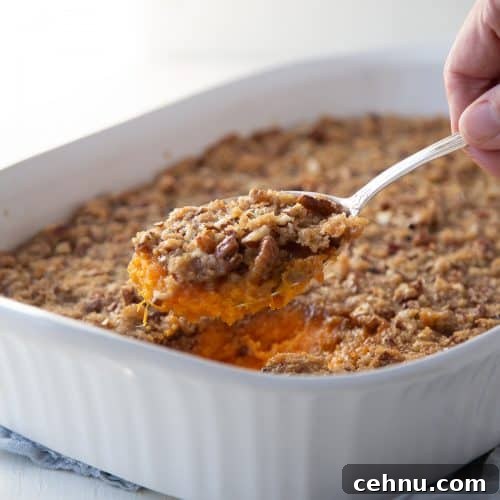 hand with a spoon of sweet potato casserole, lifting it out of a white casserole dish.
