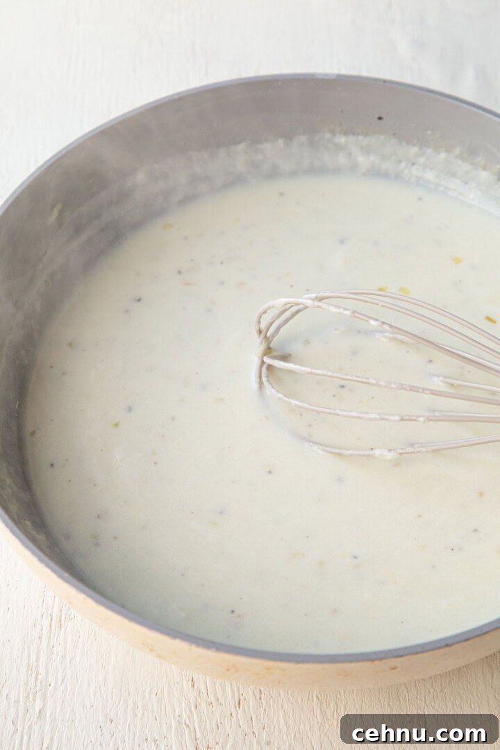 Old Fashioned Scalloped Potatoes Recipe 8 a white creamy sauce in a skillet with a whisk.