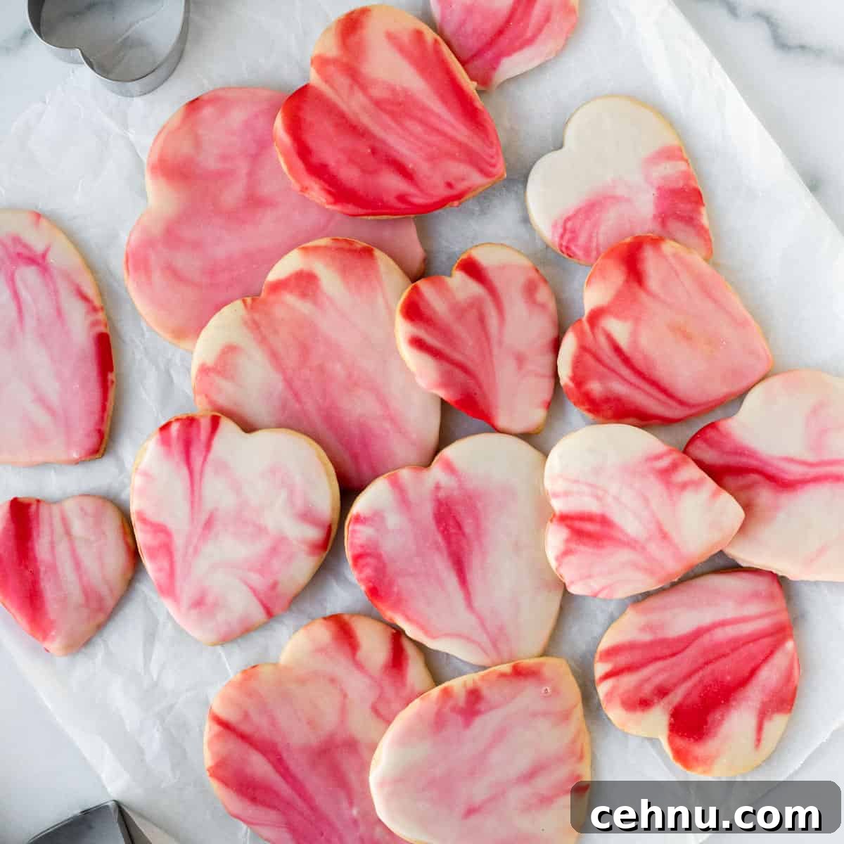 pile of red and pink marbled heart shaped sugar cookies on white parchment paper