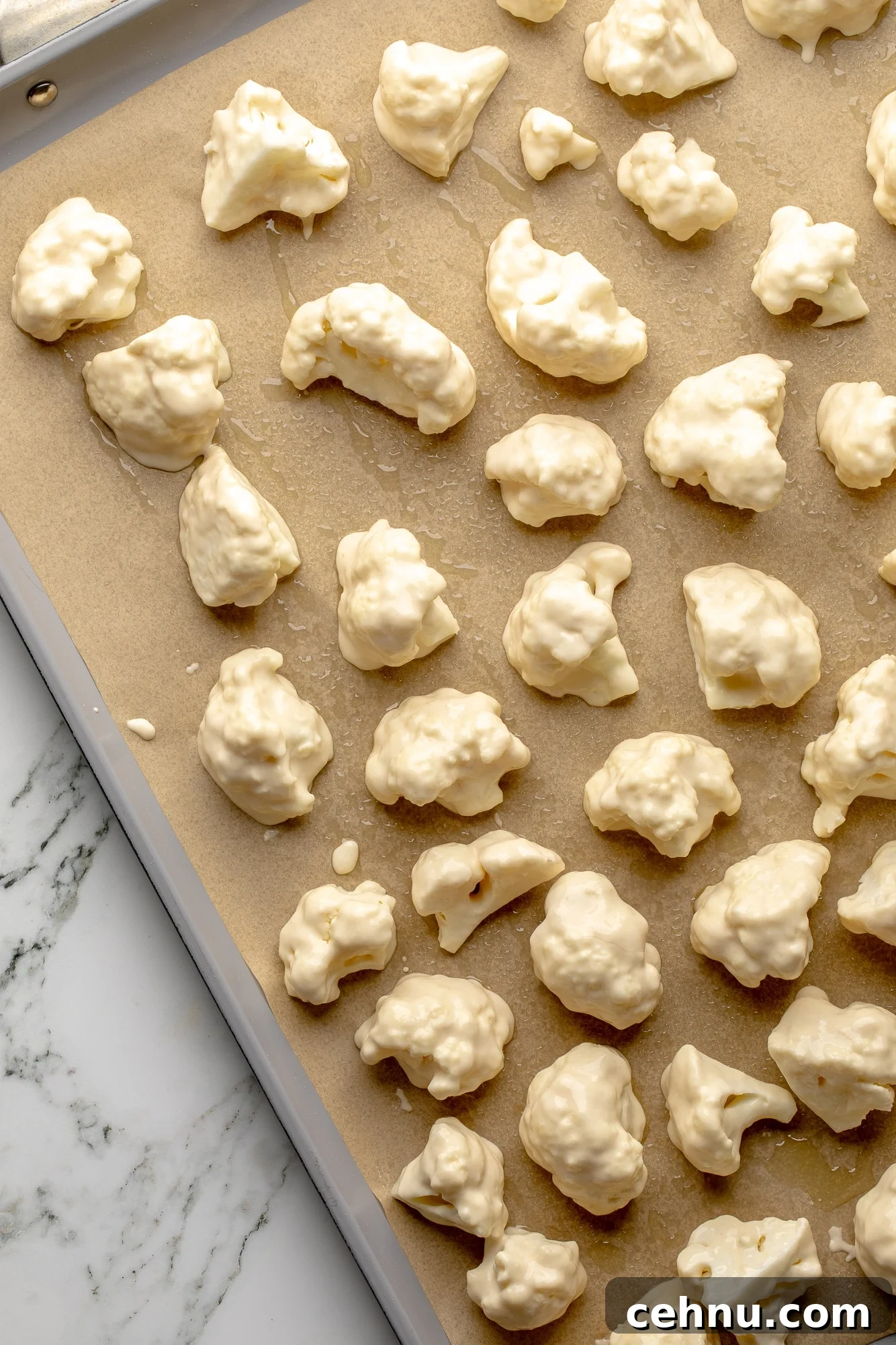 Overhead view of battered cauliflower florets on a baking sheet.