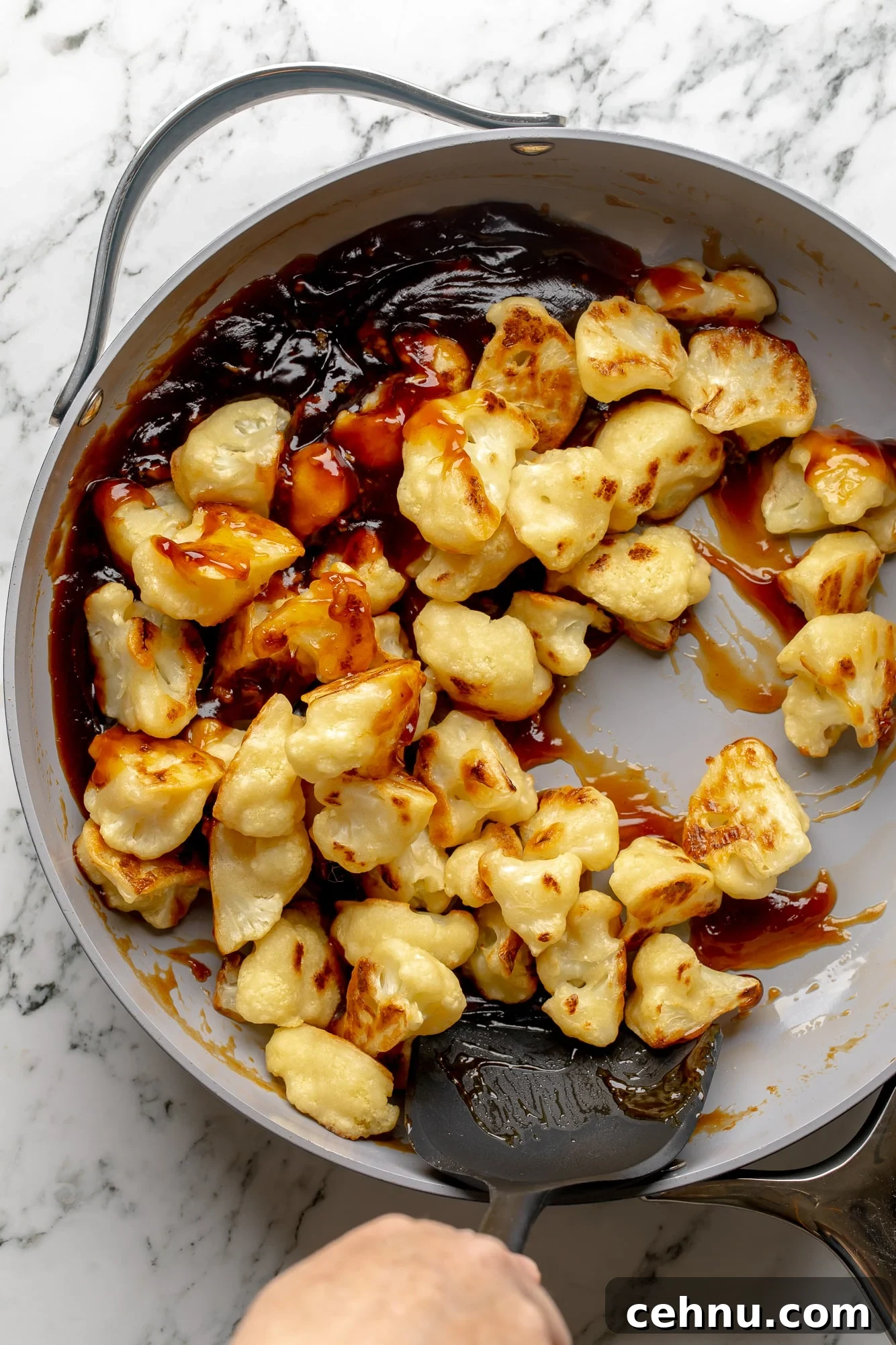 Overhead view of baked cauliflower being tossed in sesame sauce in a skillet.