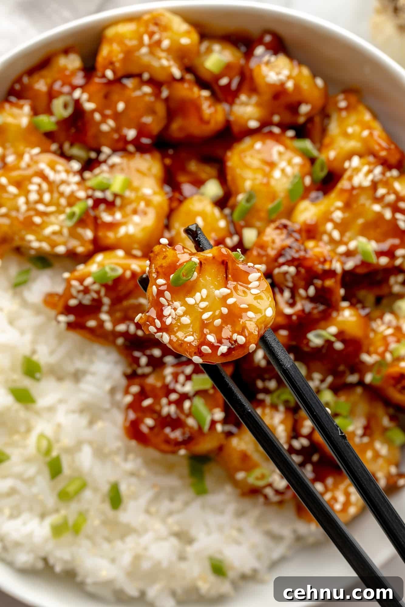 Close up on chopsticks holding a piece of sesame cauliflower.