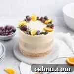 Close up of frosted three layer orange cranberry cake topped with fresh rosemary, slices of oranges and sugared cranberries.