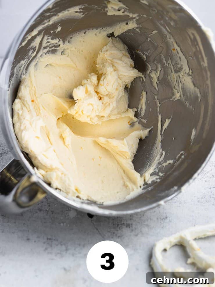 Overturned silver bowl of light yellow frosting with flecks of orange zest.