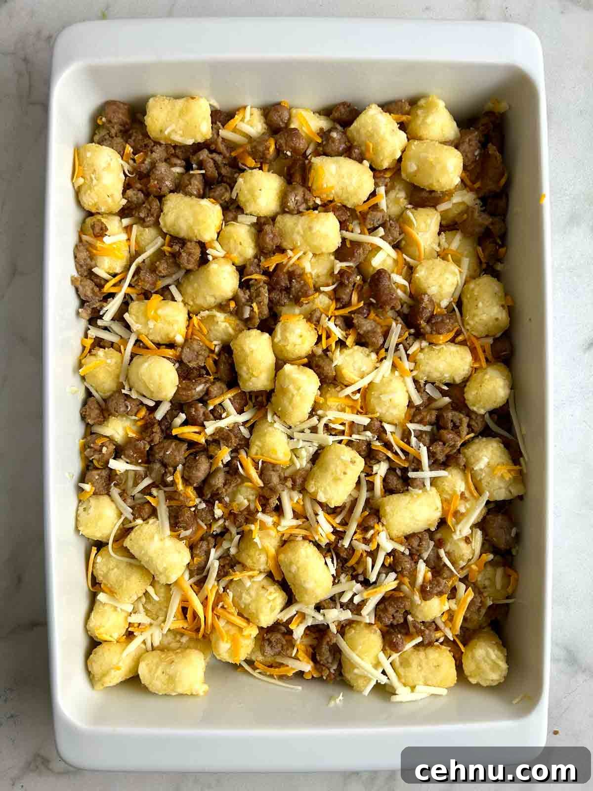 Cheesy Sausage and Tater Tot Breakfast Casserole Recipe 6 tater tots, sausage, and cheese spread in casserole dish.