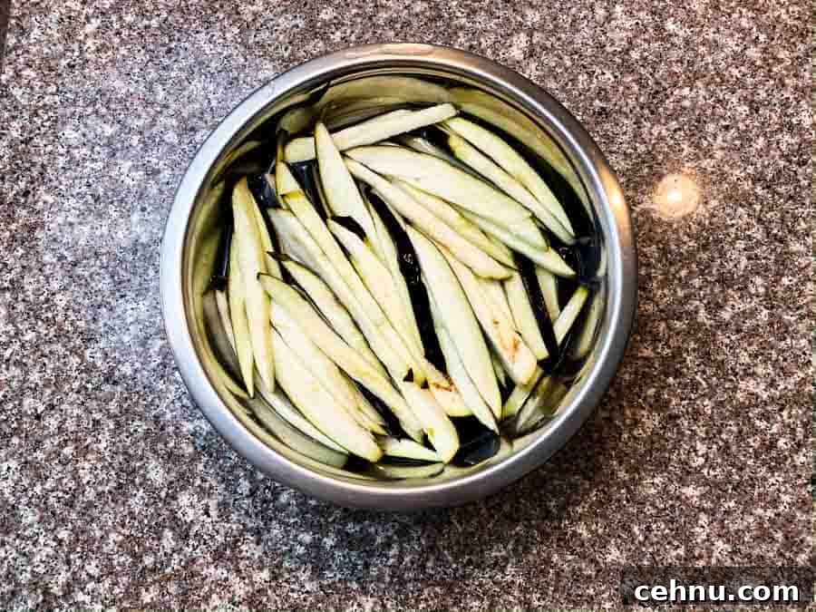 eggplant slices soaking in salt water in silver bowl