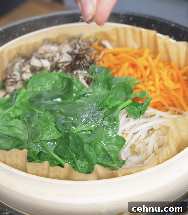 Assorted vegetables including spinach, bean sprouts, carrots, and mushrooms arranged in a steamer basket as the prep step for a healthy chicken bibimbap bowl.