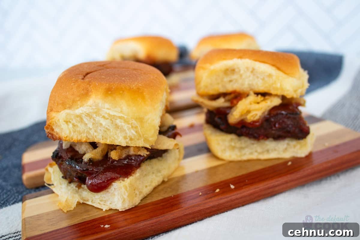 Two meatloaf sliders on a wooden board with another two behind them, featuring a Hawaiian roll, meatloaf, sauce, and fried onions.