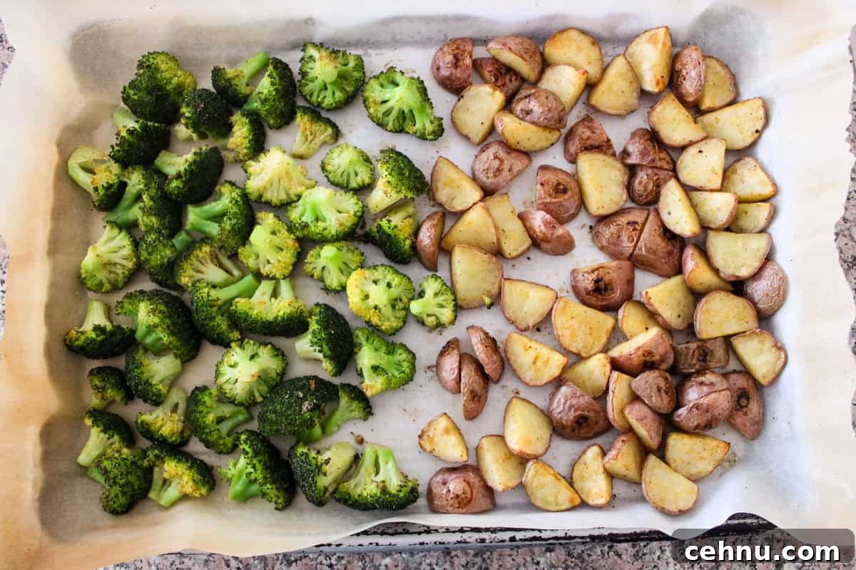 A baking tray lined with parchment paper holds roasted broccoli florets on the left and roasted potato pieces on the right, both cooked until slightly browned.