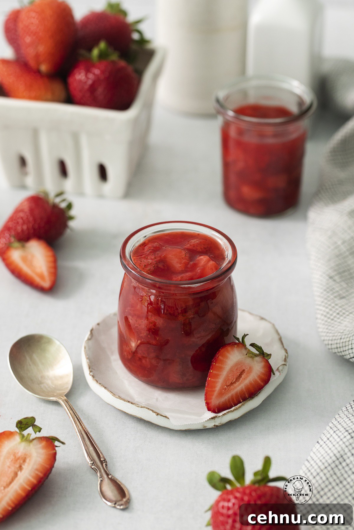 a small jar filled with homemade strawberry compote with fresh strawberries in the background.