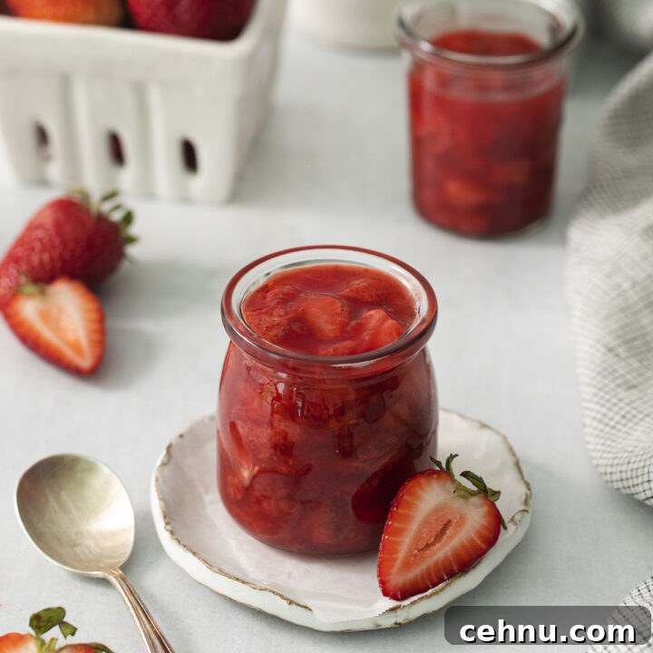 a small jar filled with homemade strawberry compote with fresh strawberries in the background.