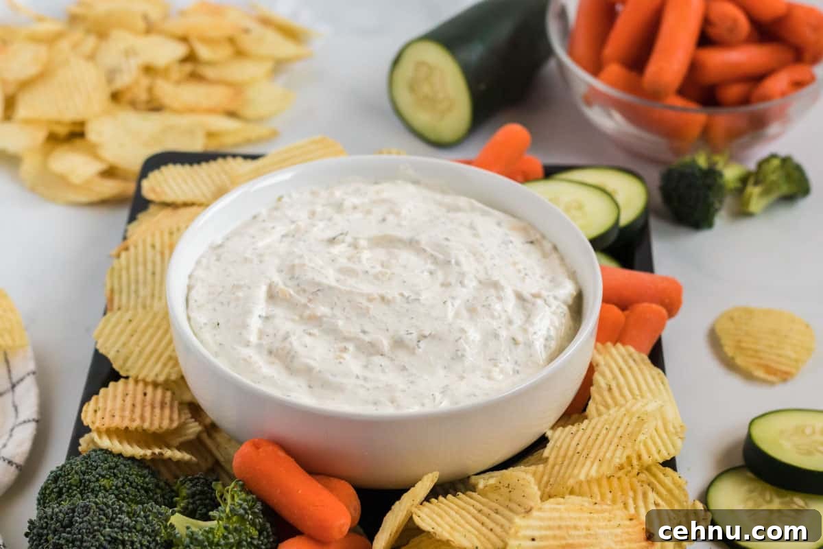 dip in a bowl surrounded by chips, broccoli, baby carrots, and cucumber