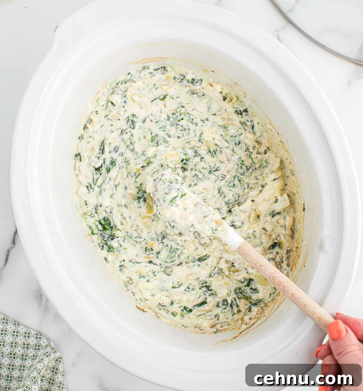 creamy slow cooker spinach artichoke dip being stirred