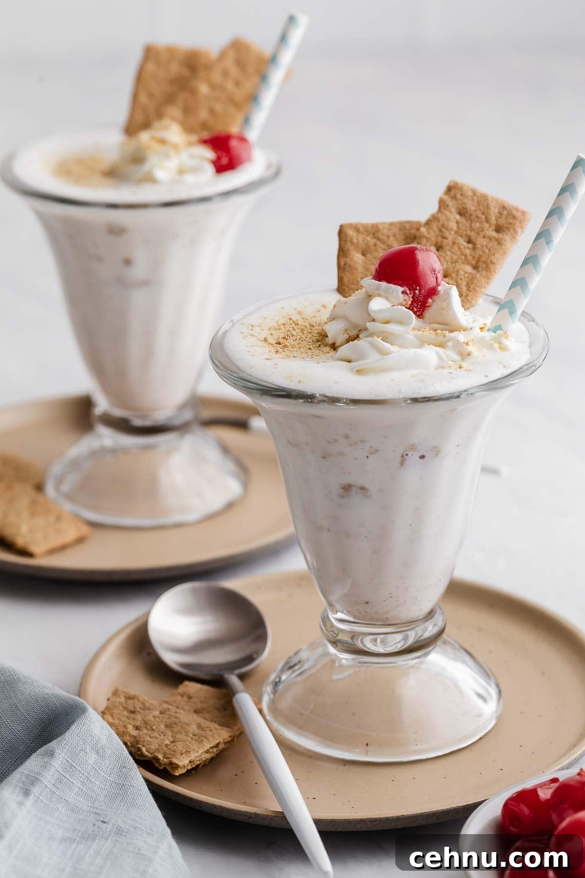Two glasses of cheesecake milkshake garnished with straws and graham crackers.
