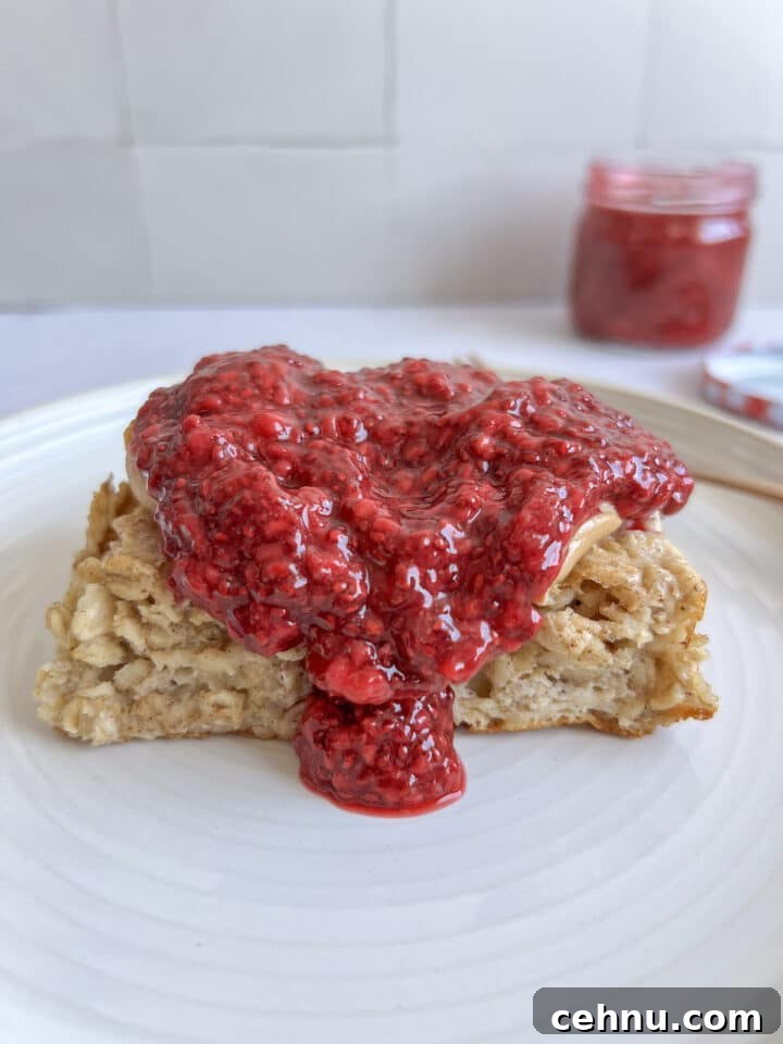 slice of baked oatmeal on a white plate, topped with peanut butter and a big dollop of chia jam
