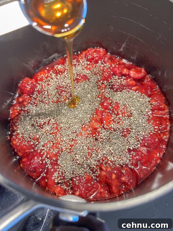 Ingredients for raspberry chia jam in a saucepan, unstirred including raspberries, chia seeds, and maple syrup