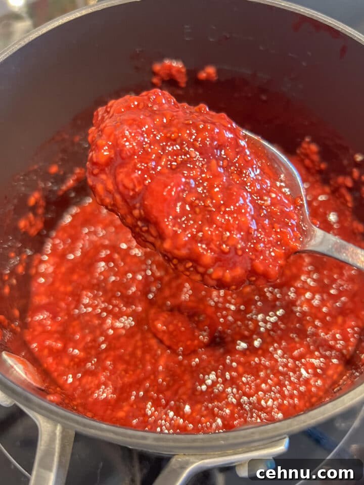 Raspberry chia jam in a black saucepan with a spoon holding some of the jam over top
