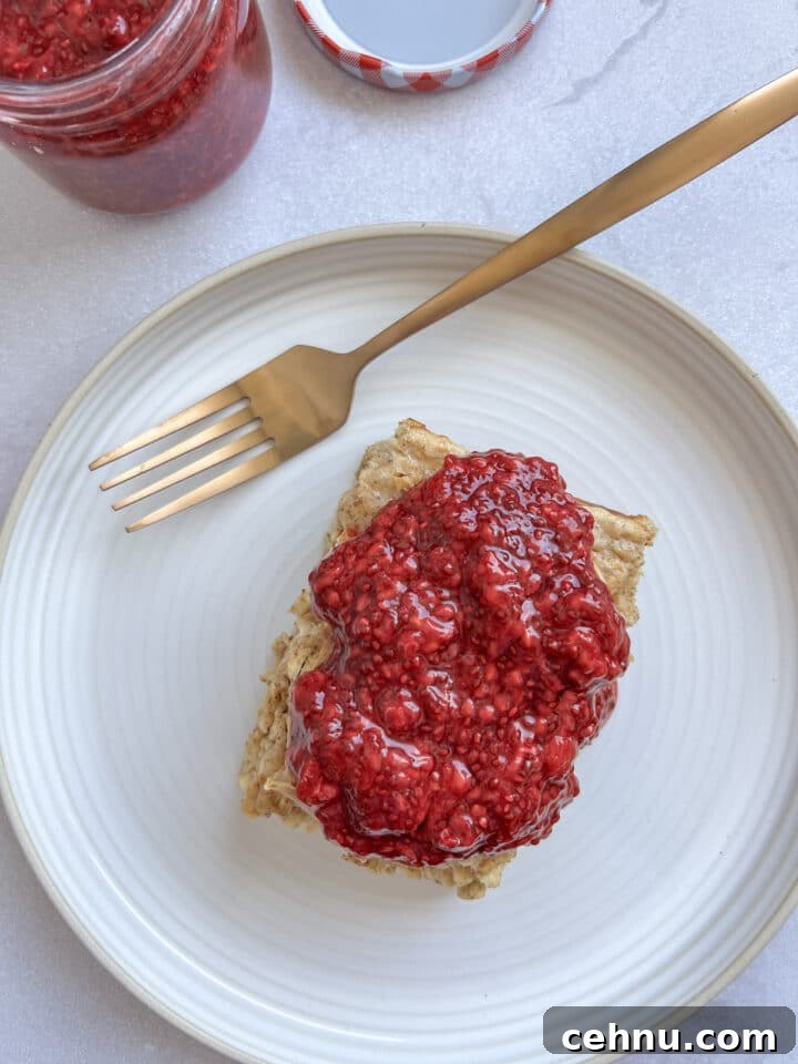 chia jam slathered on a slice of baked oatmeal, on a white plate with a gold spoon