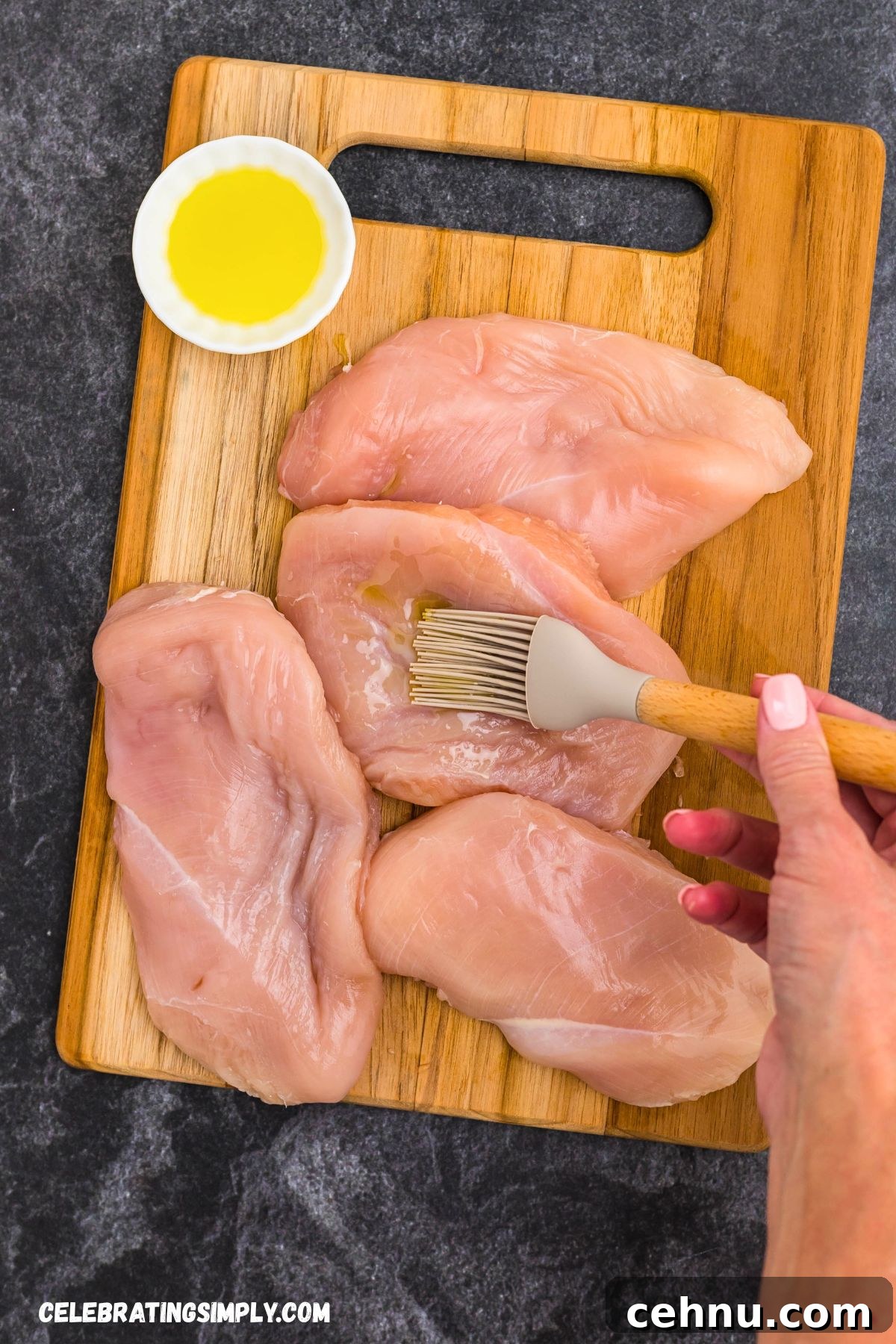 Olive oil being brushed onto uncooked chicken breasts. 