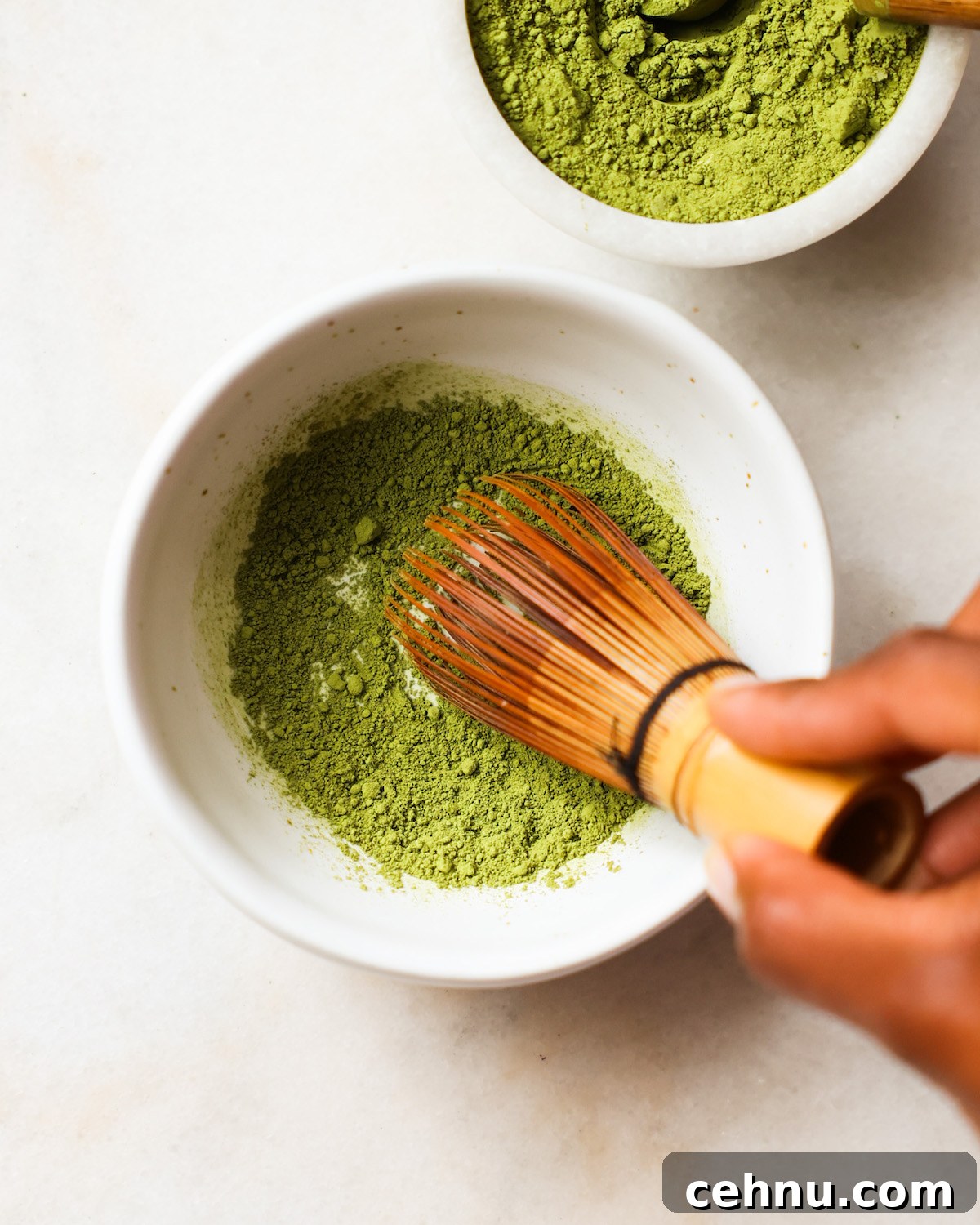 A brown hand whisking a small bowl of matcha.