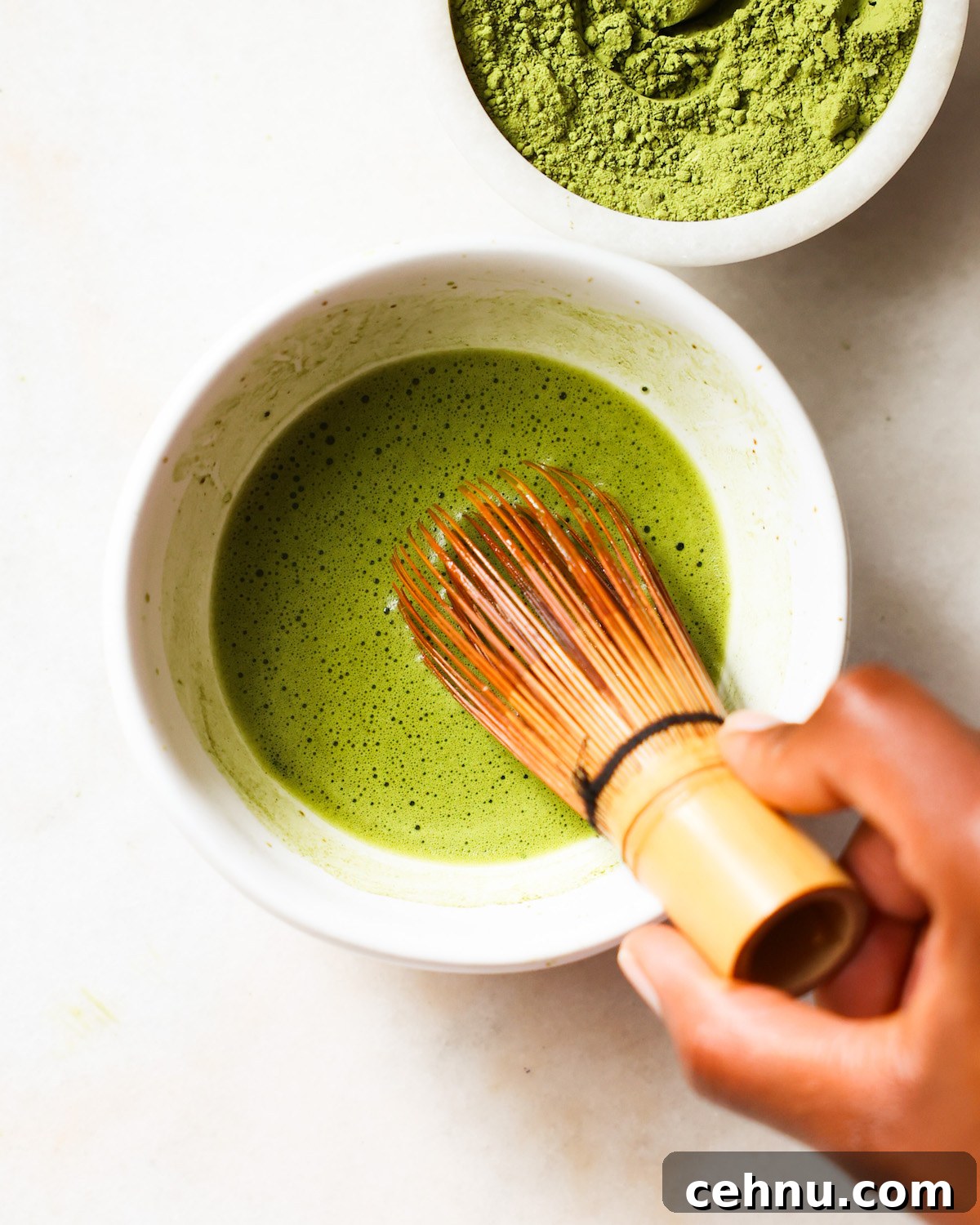 A brown hand whisking a small bowl of matcha and hot water.