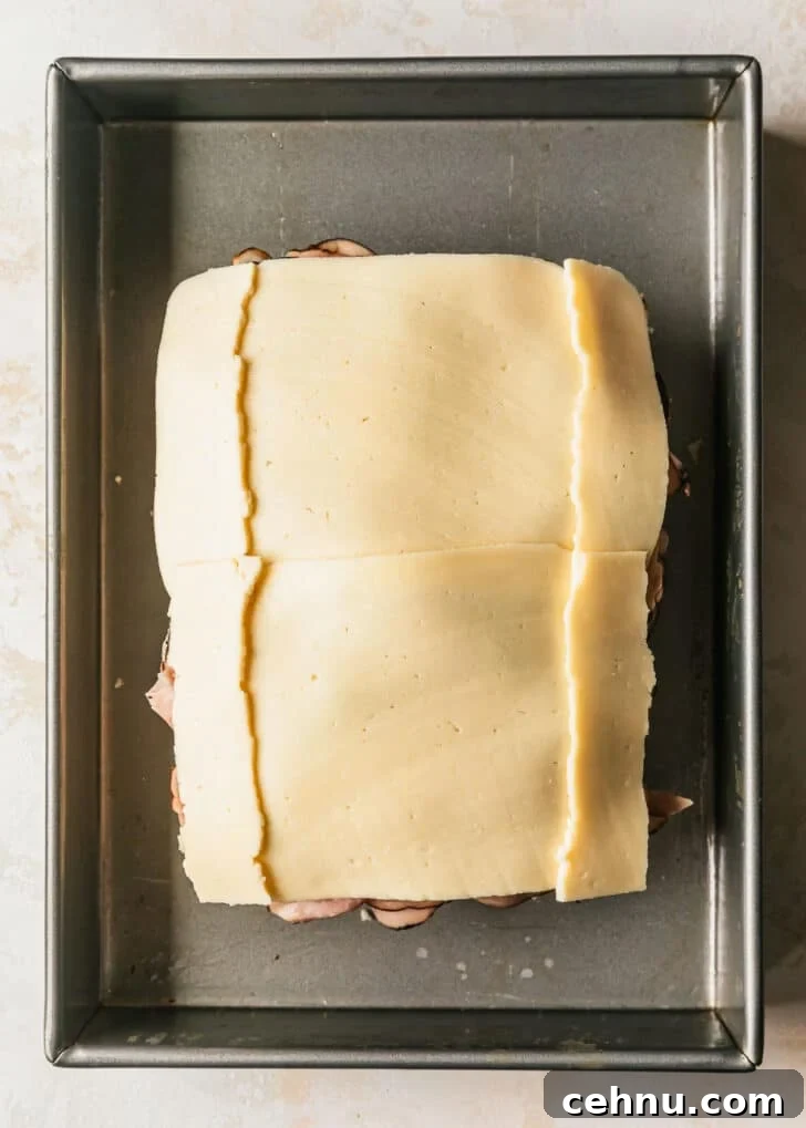 Oven-Baked Brown Sugar Ham and Melted Cheese Sliders 6 Hawaiian rolls layered with ham and havarti in a silver pan.