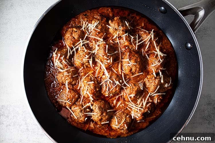 overhead view of keto meatlballs in marinara sauce topped with shredded parmesan cheese in a black skillet